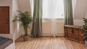 A room with a wooden floor, a bed, a dresser, a hanging lamp, and a window with green curtains. - Villa G With Pool in Lubbenau (Lübbenau/Spreewald)