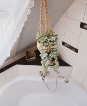 A bathroom with a white bathtub, a hanging plant, and a lace curtain. - Villa G With Pool in Lubbenau (Lübbenau/Spreewald)