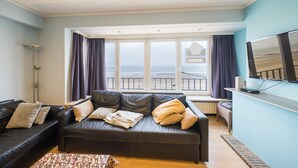 Un salon moderne doté d’une grande fenêtre, d’un canapé en cuir noir, d’un téléviseur à écran plat et offrant une vue sur la mer.