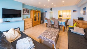 Un salon comprenant un canapé, un téléviseur, un meuble en bois et un coin repas avec des chaises et une table.