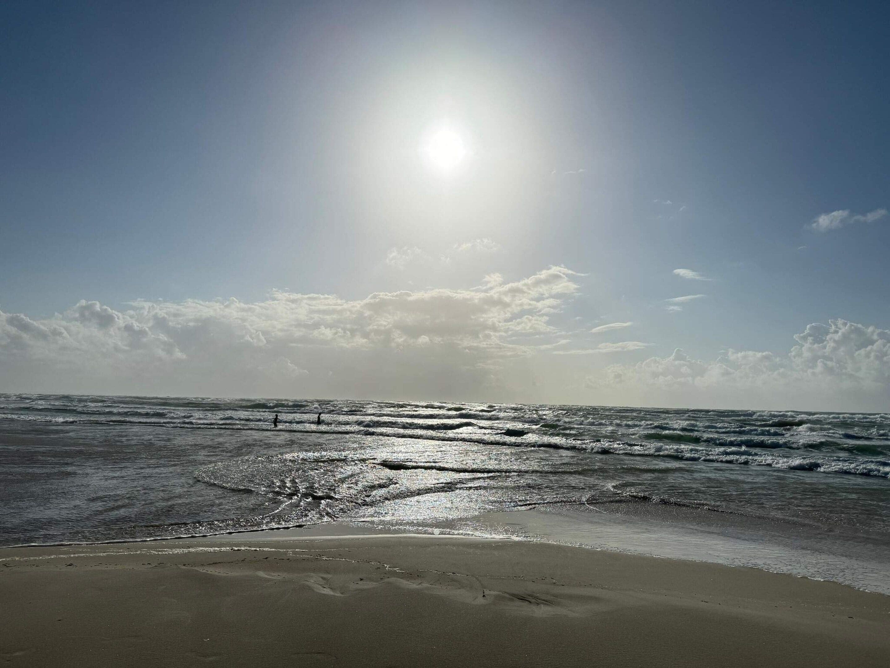 A beach with waves, a clear sky, and the sun shining.