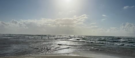 A beach with waves, a clear sky, and the sun shining.