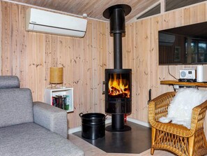 A cozy room with a wood-burning stove, a grey sofa, a wicker chair, and a bookshelf. - 4 Star Holiday Home in Lokken (Lokken)
