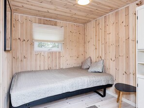 A room with a bed, a window, a small table, and wooden walls. - 4 Star Holiday Home in Lokken (Lokken)