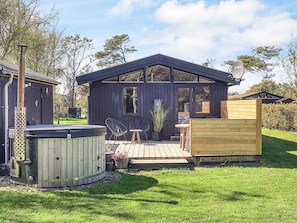 A wooden cabin with a hot tub, outdoor seating, and a deck.