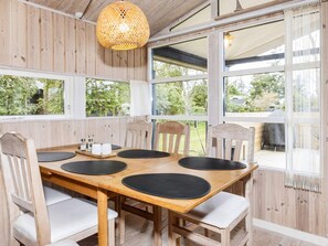 A wooden dining table with six chairs, a woven light fixture, and large windows with a view of greenery. - 4 Star Holiday Home in Lokken (Lokken)