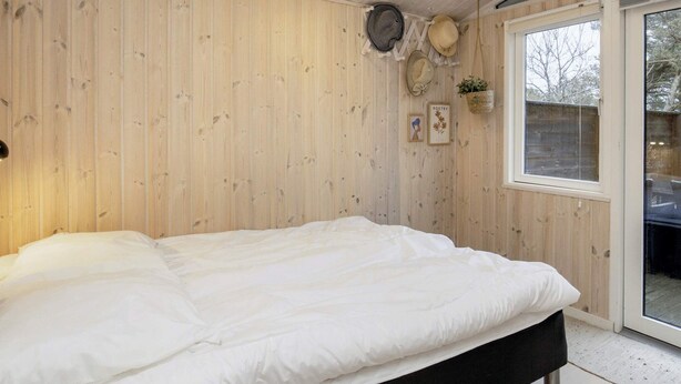 A bedroom with a bed, wooden walls, a window, and a ceiling light.