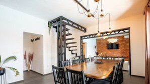 Un espace repas moderne avec une table en bois et des chaises noires, un mur d’accent en briques et un escalier à la structure métallique.