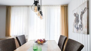 A dining room with a wooden table, wicker chairs, a fruit bowl, and a hanging light fixture. - on the Sunny Slope Modern Retreat (Eslohe)