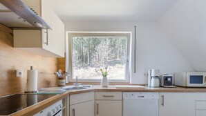 A modern kitchen with a wooden countertop, stainless steel appliances, and a window with a forest view. - on the Sunny Slope Modern Retreat (Eslohe)
