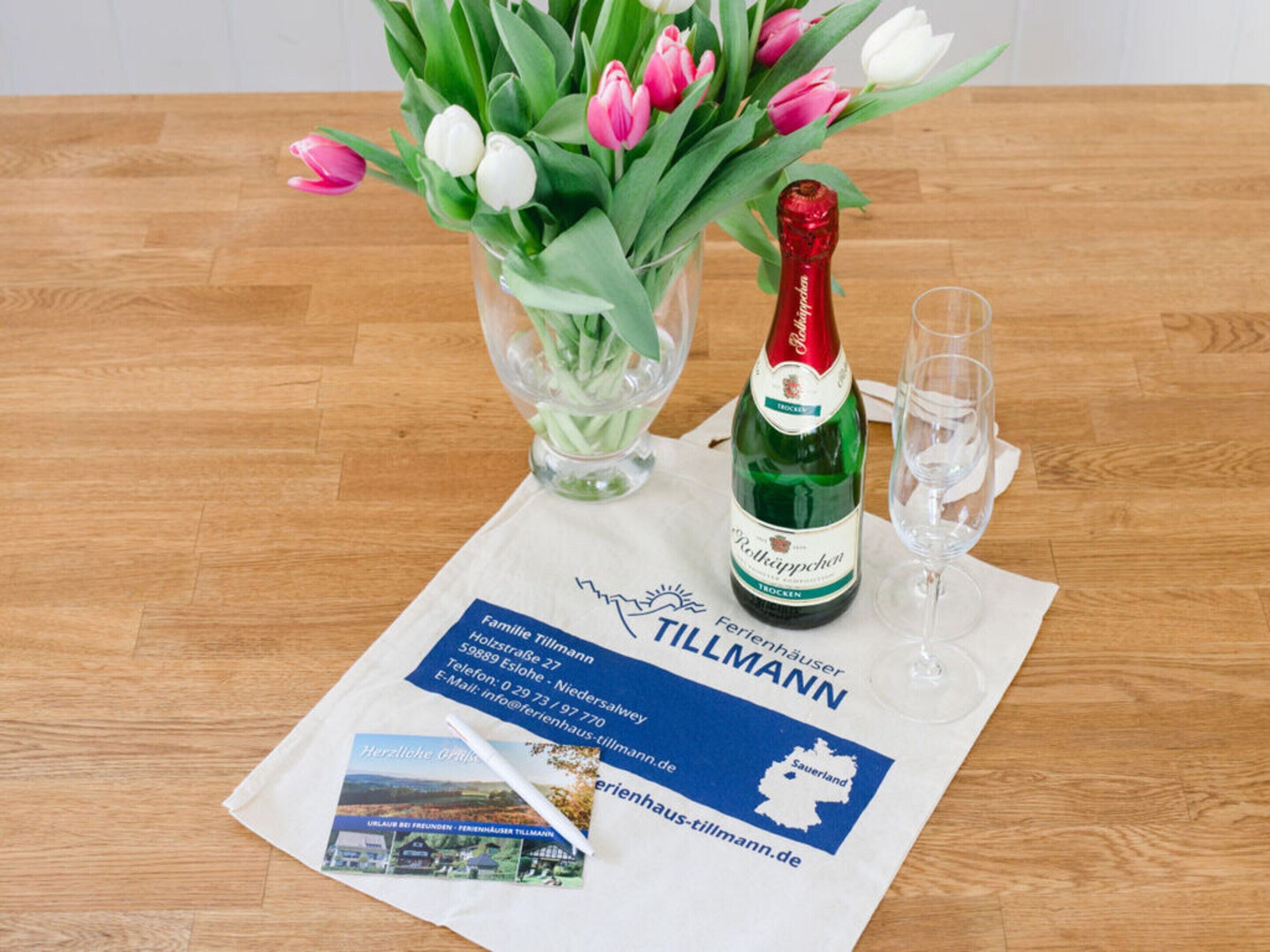 A wooden table with a bottle of Rottkappechen, a glass, and a brochure for a hotel named Tillmann.