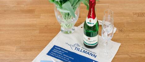 A wooden table with a bottle of Rottkappechen, a glass, and a brochure for a hotel named Tillmann.