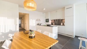 Een moderne keuken met witte kastjes, een houten eettafel en een hanglamp.