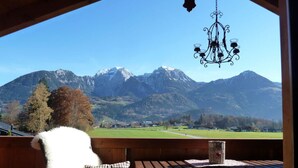 A view from a balcony with a wooden table, a chair, and a chandelier. - Konigssee - Reich Family (Schoenau am Koenigssee)
