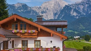 A traditional chalet with wooden balconies adorned with flowers, set against a mountainous backdrop. - Konigssee - Reich Family (Schoenau am Koenigssee)