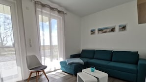 A modern living room with a teal sofa, a white coffee table, and a wooden chair. - Holiday Apartment Lotte Een (Zingst)