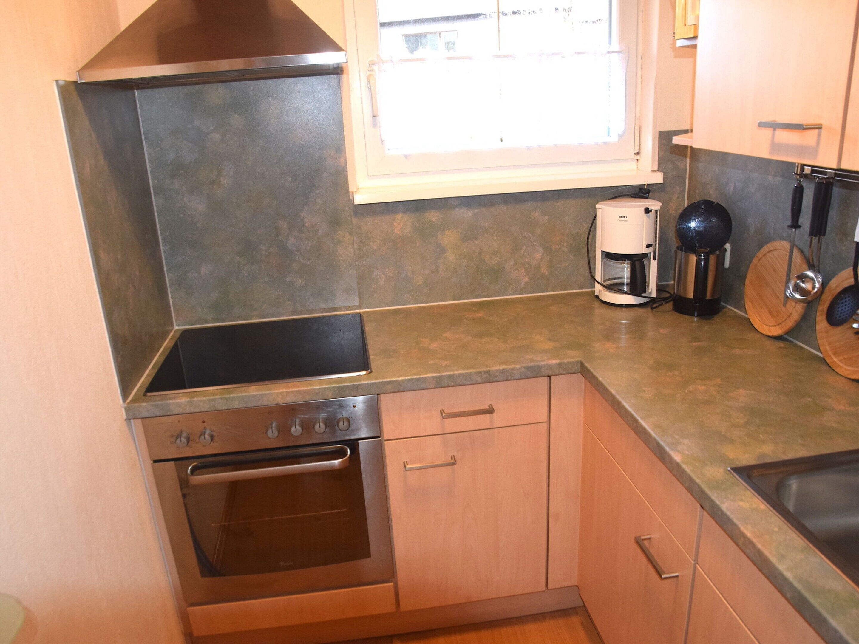A compact kitchen with a stainless steel range, a built-in oven, wooden cabinets, and a window providing natural light.