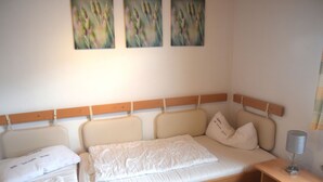 A bedroom with a wooden headboard, a bed with white bedding, a bedside table with a lamp, and three wall-mounted paintings. - Lakeside Comfort in Fussen (Fuessen)