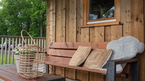 A wooden bench with woven cushions and a basket with flowers on a wooden deck.
