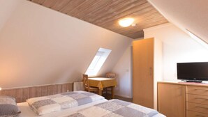 A bedroom with two beds, a wooden ceiling, a TV, and a desk with a chair. - Holiday Home Villa Piep (Nebel)