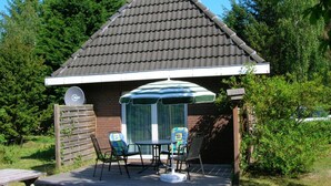A house with a tiled roof, a satellite dish, a covered patio with a table and chairs, and a wooden fence. - Holiday Home Villa Piep (Nebel)