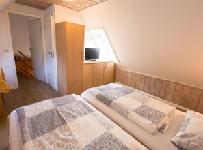 A bedroom with two beds, a wooden wardrobe, a television on a stand, and a window providing natural light. - Holiday Home Villa Piep (Nebel)