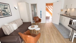 A modern living room with a brown sofa and leather chairs, a small white table, and a kitchen area with cabinets and a sink. - Holiday Home Villa Piep (Nebel)