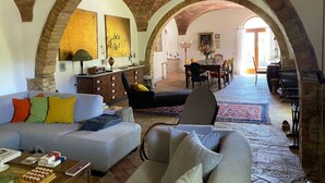 Un saló espaiós amb un sostre alt i arquejat, un conjunt de sofàs, una taula de dinar amb cadires i una vista a través d'una arcada cap a una altra habitació.