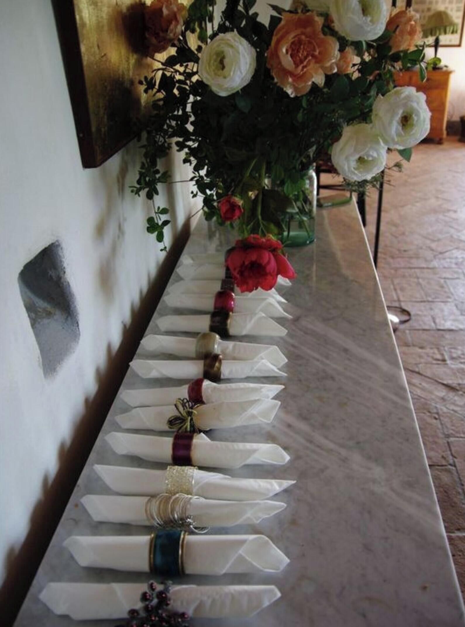 A marble table with neatly folded white napkins, some with decorative ribbons and beads, and a vase of flowers on the right.