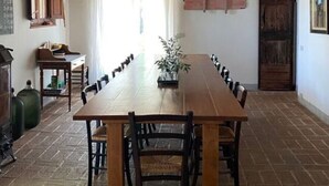 Zona de menjador amb una taula de fusta llarga, cadires i un penjador d'il·luminació.