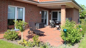 Une maison en briques avec un toit en tuiles, un patio couvert avec des meubles d’extérieur et un barbecue.