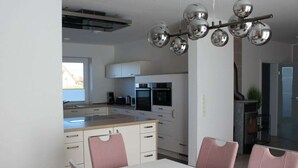 Une cuisine moderne avec des meubles blancs, un îlot central et un coin repas avec des chaises roses.