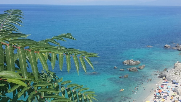Ein Strand mit klarem türkisblauem Wasser, Felsenformationen und üppigem Grün im Vordergrund.