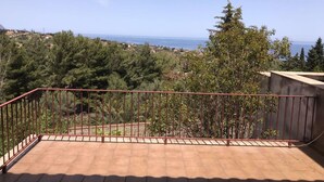 Ein Balkon mit Metallgeländer, der auf eine Küstenlandschaft mit Bäumen und Gebäuden blickt.