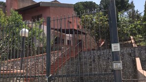 Eine durch eine Steinmauer und ein Metallgitter geschützte Anlage mit einer Treppe, die zu einem roten Gebäude führt.