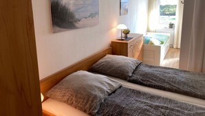 Un dormitorio con dos camas, una mesita de noche, una lámpara y una ventana con cortinas.