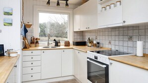Una cucina con mobili bianchi, un piano di lavoro in legno, un forno integrato e una finestra con vista sugli alberi.