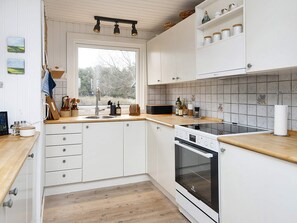 Una cocina con armarios blancos, encimera de madera, horno empotrado y ventana con vistas a árboles.