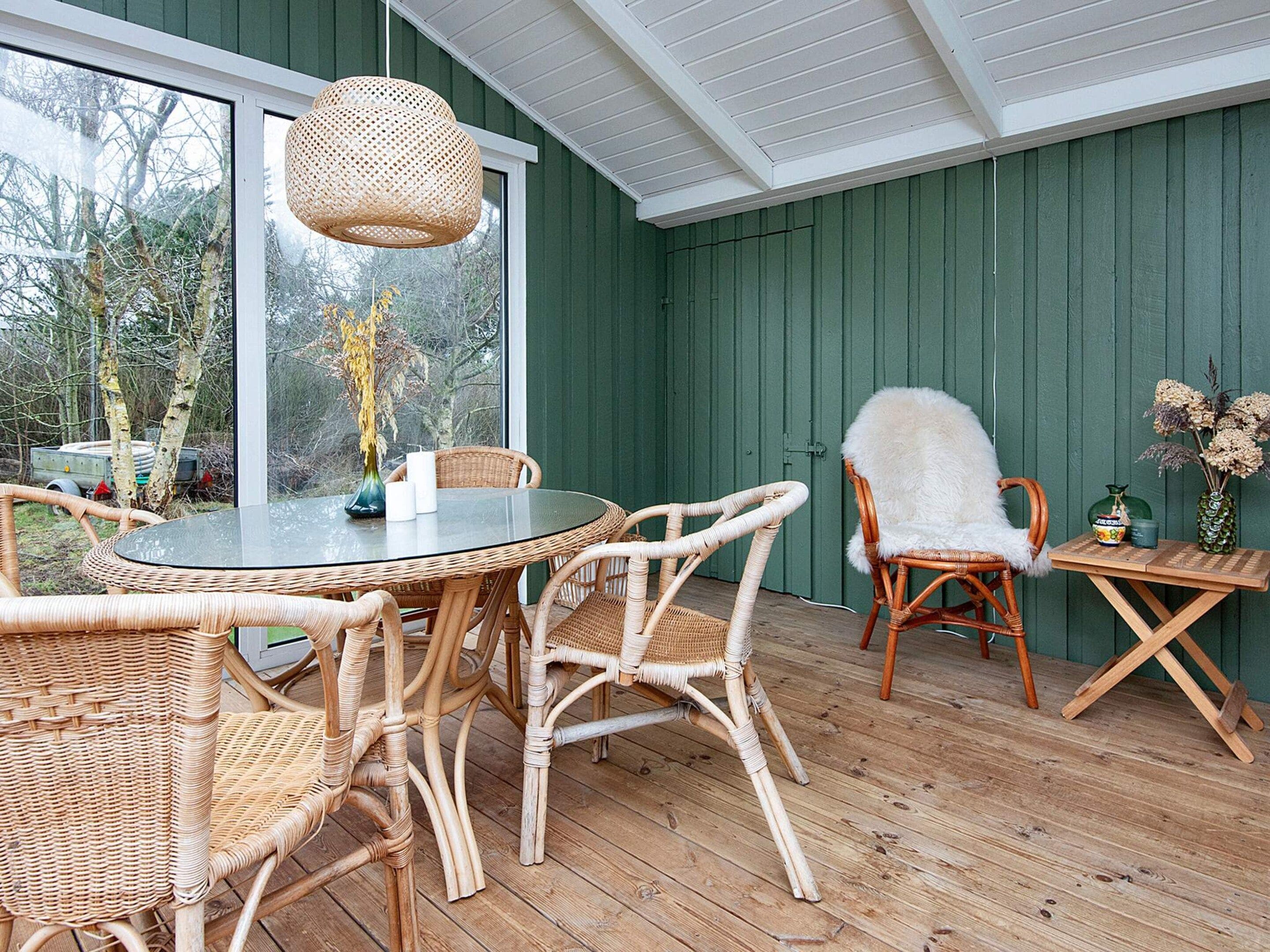 A room with a round glass table surrounded by wicker chairs, a white furry chair, and a small wooden table with a vase.