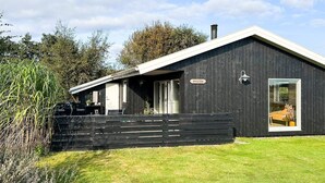 Un bâtiment moderne de couleur noire, doté d’un toit en pente, d’une grande porte vitrée et d’une enseigne sur laquelle on peut lire « KNASTEN ».