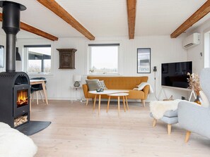 Una sala de estar moderna con una estufa de leña, un sofá, un televisor y una zona de comedor.