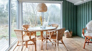 A room with a round table and wicker chairs, large windows, and a view of trees. - 4 Star Holiday Home in Fano (Fano)
