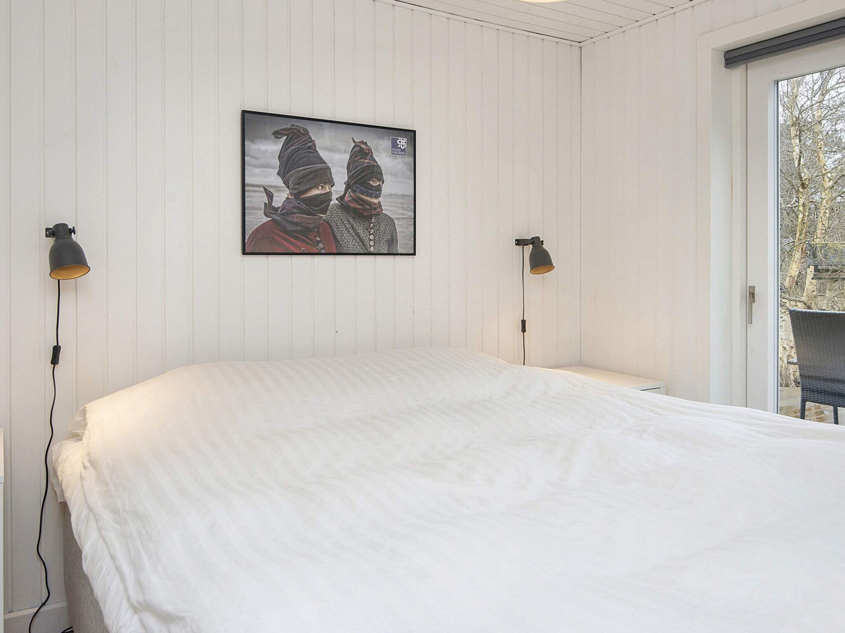 Une chambre à coucher avec un lit, deux lampes fixées au mur et un tableau encadré accroché au mur.