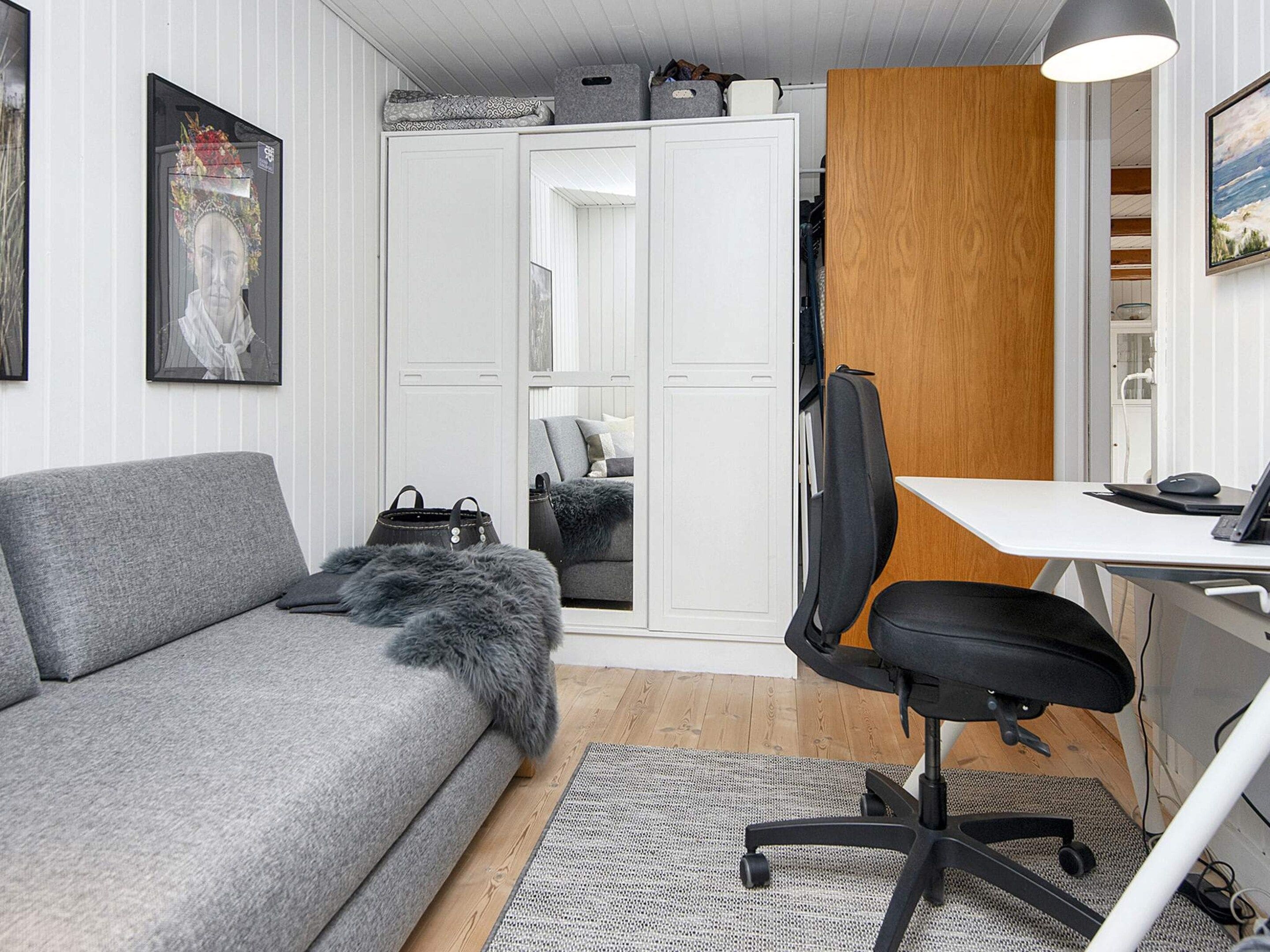 A modern room with a grey sofa, a black office chair, a wooden desk, and a white wardrobe.