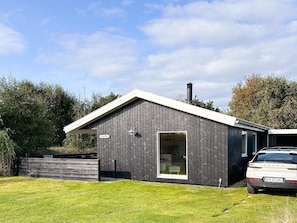 A modern building with a dark exterior, a visible chimney, and a car parked in front.