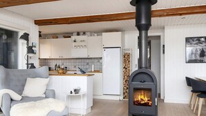 A cozy living room with a grey sofa, a white furry ottoman, and a black wood-burning stove. - 4 Star Holiday Home in Fano (Fano)