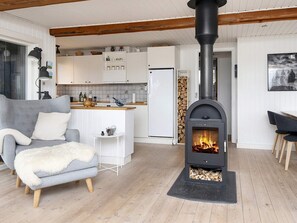 A cozy living room with a grey sofa, a white furry ottoman, and a black wood-burning stove. - 4 Star Holiday Home in Fano (Fano)