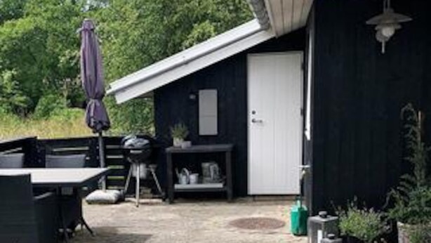 Katettu ulkotila, jossa on pöytä ja tuoleja, riippuvalaisin ja ovi rakennukseen.