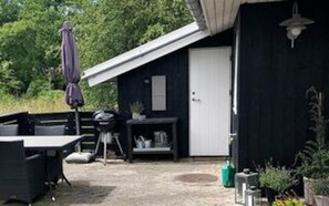 A covered outdoor area with a table and chairs, a hanging light fixture, and a door to a building. - 4 Star Holiday Home in Fano (Fano)