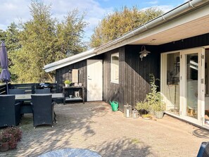 Ein Holzhaus mit einer Terrasse, Gartenmöbeln und einer Glastür.